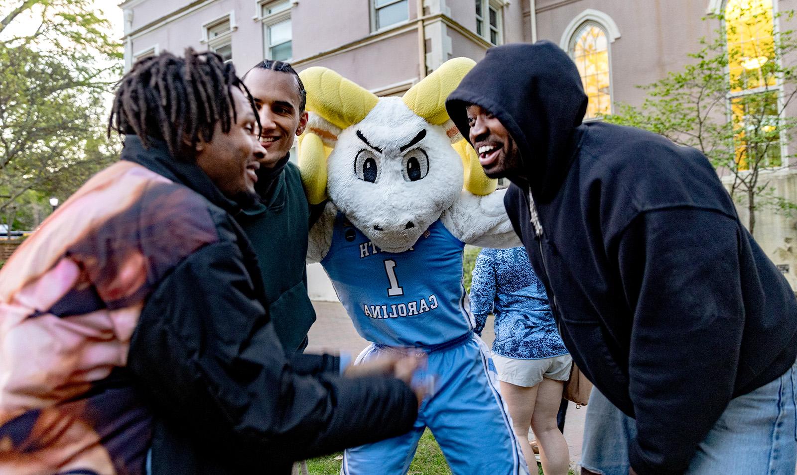 The UNC-Chapel Hill ram mascot, Rameses, huddled with three students.