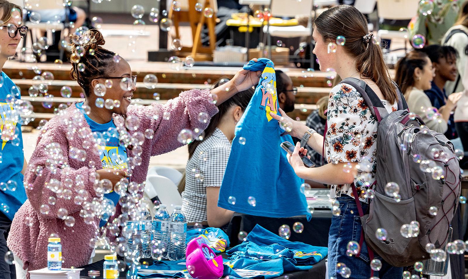 Bubbles floating in the air as a student is handed an Arts Everywhere T-shirt.