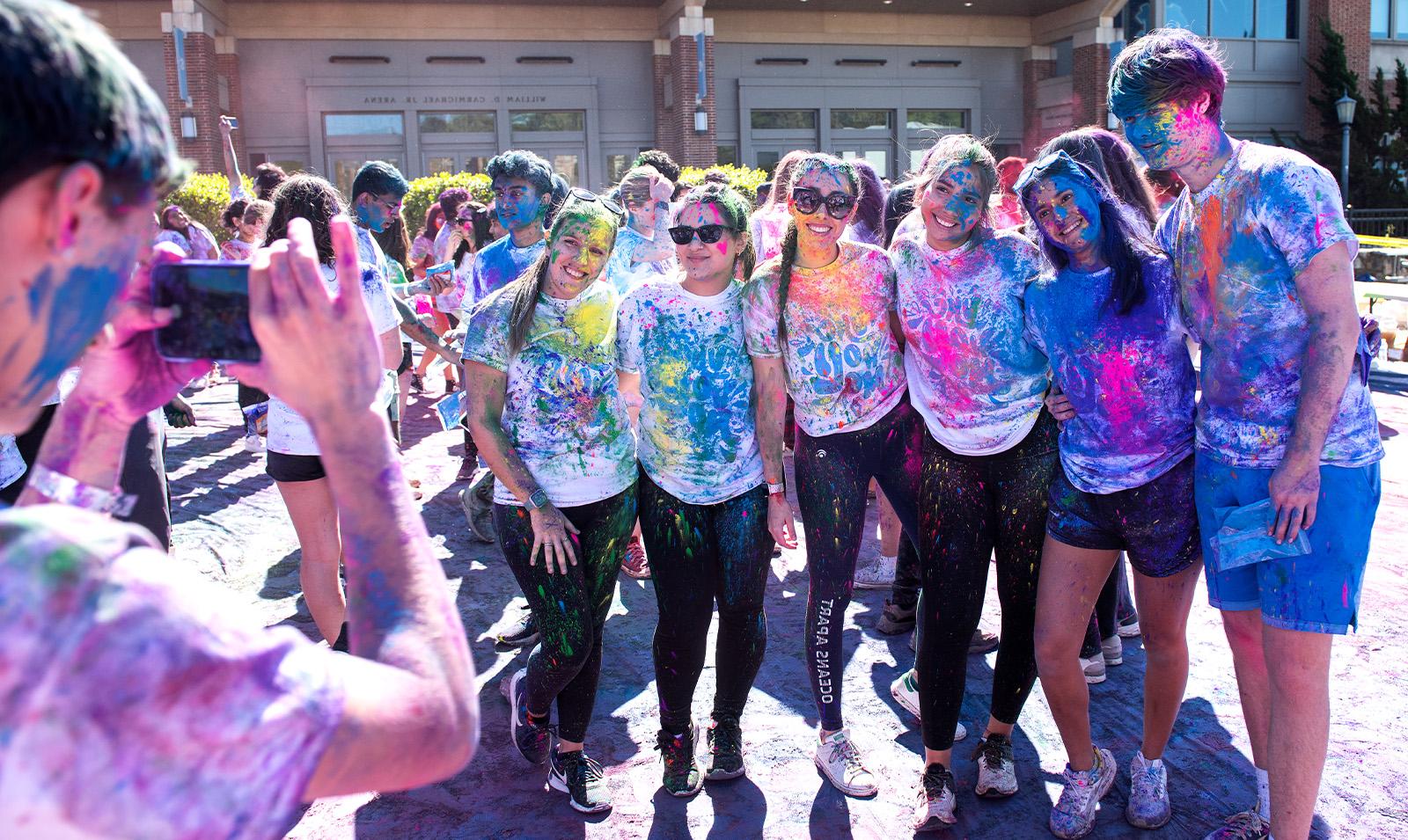 Crowd of students covered in paint celebrating Holi and posing for a group photo.