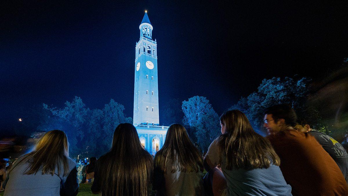 Students watching the lighting of the Bell Tower Carolina Blue at night the day before the first day of classes.